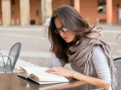 眼鏡をかけた外人女性がカフェで本を読んでいる